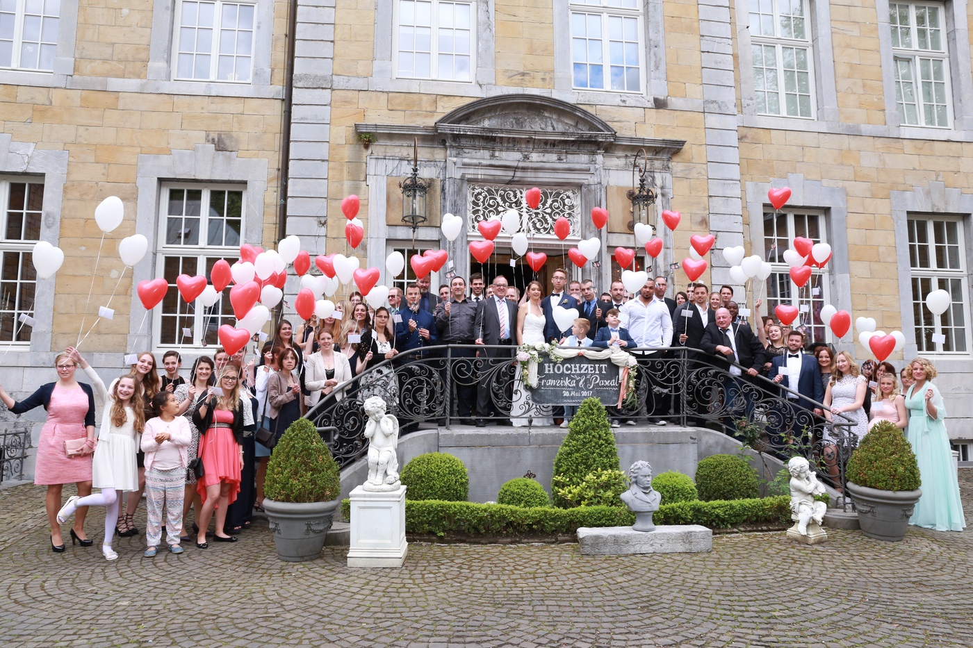 Hochzeitsgesellschaft mit Luftballons vor dem Schloss